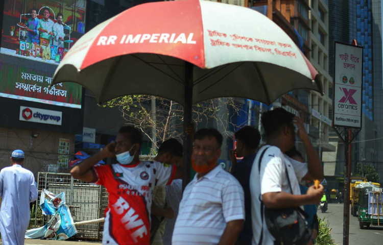 একটু স্বস্তির জন্য যেখানে ছায়া মিলছে সেখানেই দাঁড়ানোর চেষ্টা করছেন পথচারীরা। ছবি: মাহবুব আলম