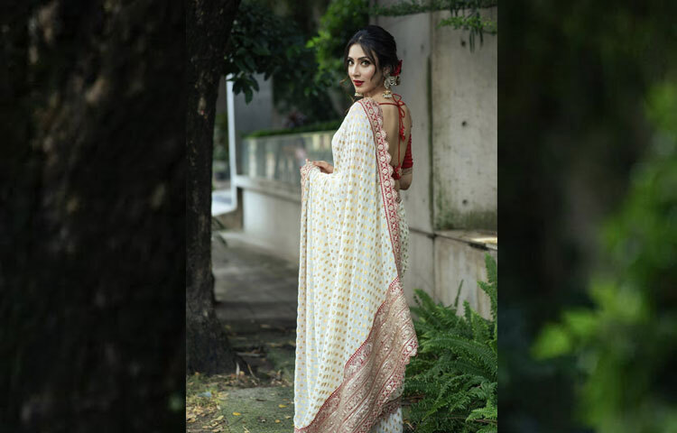 সাদা জমিনে সোনালি মোটিফের নকশা, তার সঙ্গে লাল পাড়জুড়ে ঝলমলে সোনালি সিকুইনের কাজ-পুরো আভিজাত্য যেন এক ফ্রেমেই ধরা দিয়েছে।