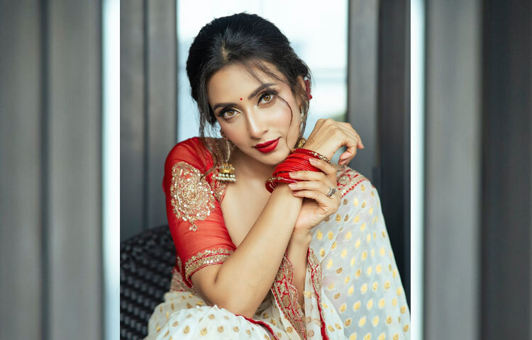 শাড়ির সঙ্গে মিলিয়ে হাতে লাল চুড়ির গোছা, কানে ঝুলানো বড় ঝুমকা আর খোঁপায় গুঁজে দেওয়া লাল গোলাপ-সবকিছু মিলেই তার সাজে যুক্ত হয়েছে এক পূর্ণতা।