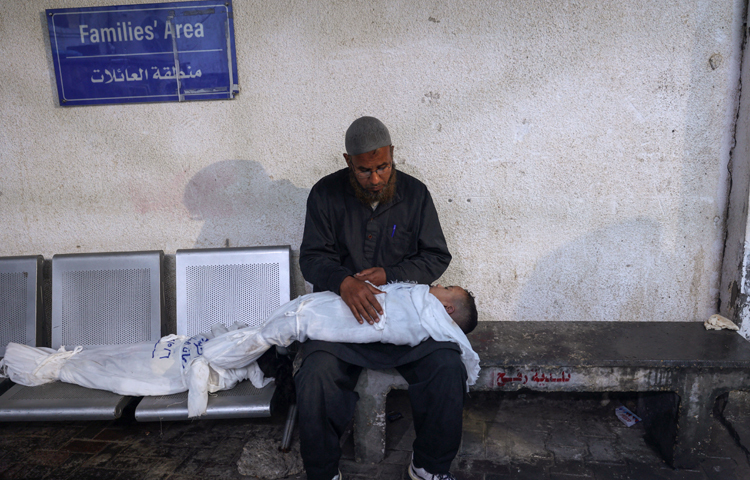 সন্তানের নিথর দেহ নিয়ে হাসপাতালের করিডোরে বসে আছেন অসহায় বাবা। ছবি: এএফপি