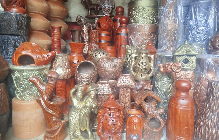 বিকেলের ম্লান আলোয় দোয়েল চত্বর। চারপাশে ব্যস্ত মানুষের ভিড়, তবু আলাদা করে চোখে পড়ে রঙিন একঘর পসরা। সারি সারি সাজানো কলসি, হাঁড়ি, ফুলদানি, শো-পিস, কাপে-গ্লাসে ঢাকা দেওয়া লালচে আভা। মাটির গন্ধ মিশে আছে বাতাসে।