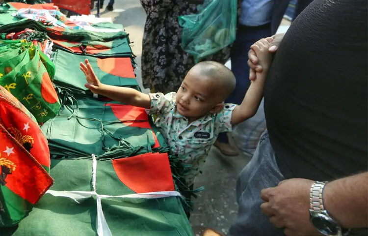 গুলিস্তানের ফুটপাত ধরে হাঁটলেই দেখা যায়, হাতের তৈরি কাপড়ের পতাকা থেকে শুরু করে লাল–সবুজ ব্যান্ড, কাগজের ব্যাজ, শিশুদের জন্য ছোট টুপি সবই সাজিয়ে রেখেছেন দোকানিরা।