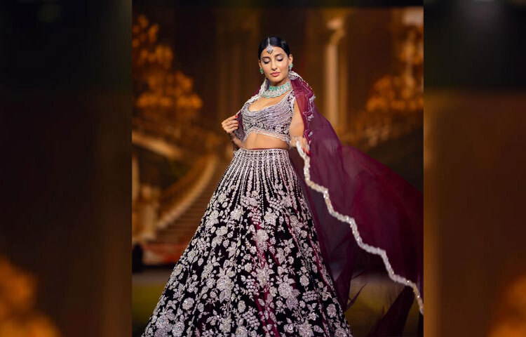 গাঢ় গারনেট ভেলভেটের ওপর সোনালি-রুপালি জরির কারুকাজে তৈরি লেহেঙ্গা নোরাকে এনে দিল রাজকীয় আভিজাত্যের রূপ।