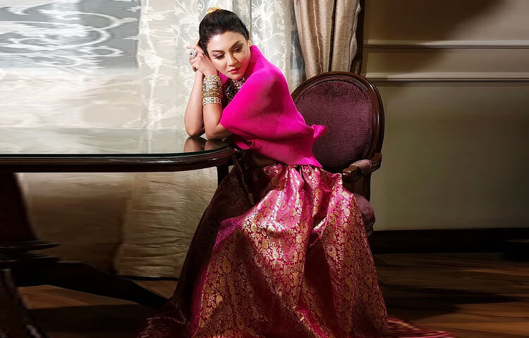 এর সঙ্গে মিলিয়ে পরেছেন ডিপ-নেক ডিজাইনের ব্লাউজ, যা পুরো লুকটিতে এনে দিয়েছে সাহসী এক আধুনিক স্পর্শ। ব্লাউজের ওপরে লেয়ার হিসেবে হট পিংক রঙের কেপটি তার সাজে যুক্ত করেছে ফিউশন ফ্যাশনের নতুন মাত্রা।