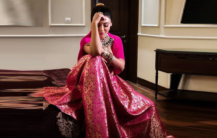 তার পরনে ছিল ঐতিহ্যবাহী বেনারসি ফেব্রিকের স্কার্ট, যার ওপরের অংশে ফুটে উঠেছে সূক্ষ্ম ফুলেল নকশা। স্কার্টটির মেজেন্টা আর সোনালি টোন যেন একসঙ্গে বয়ে এনেছে ঐতিহ্যের গাম্ভীর্য আর ফ্যাশনের উজ্জ্বলতা।