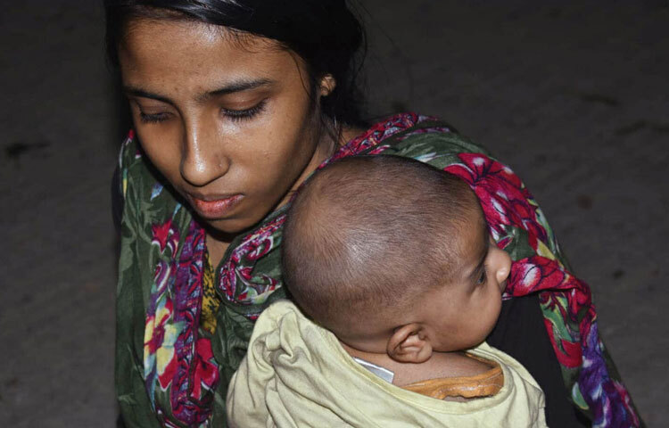 একজন মা বসে এক হাতে তার ঘুম না আসা শিশুকে জড়িয়ে রেখেছেন, আরেক হাতে চোখ মুছছেন।