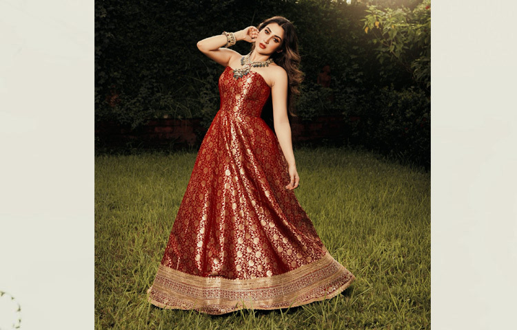 ফ্লোর-লেংথ লাল-সোনালি জ্যাকার্ড ফেব্রিকের স্ট্র্যাপলেস কোরসেট গাউনে যেন রাজকীয় আভা ছড়িয়ে দিলেন ঐন্দ্রিলা। গাউনের প্রতিটি ভাঁজে ফুটে উঠেছে সোনালি ফুলেল কারুকাজ, যা পুরো লুককে দিয়েছে জমকালো ছোঁয়া।