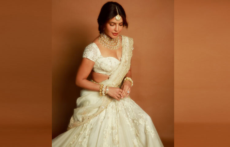 তার গহনা যেন পুরো সাজের ভাষা হয়ে উঠেছে। বড় আকারের চোকার নেকলেস, কপালের টিকলি, ঝুমকা এবং হাতে পরা ভারী গোল্ড ব্রেসলেট সব মিলিয়ে এক রাজকন্যাসুলভ আবেদন তৈরি করেছে। প্রতিটি গয়নাতে খচিত সূক্ষ্ম অলঙ্করণ যেন সোনার ভেতর গল্প আঁকে।