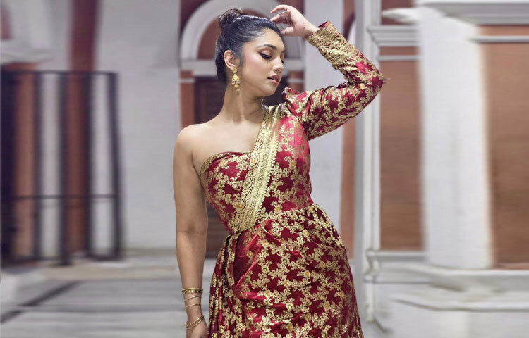 গাঢ় লাল আর সোনালি ঝলমলে কারুকাজে সাজানো এই ওয়ান শোল্ডার গাউনটি তৈরি হয়েছে ঐতিহ্যবাহী কাতান শাড়ির বুনন থেকে। সূক্ষ্ম জরির ফুলেল নকশা ও নিখুঁত ফিটিং যেন পোশাকটিকে দিয়েছে এক ভিন্ন মর্যাদা।