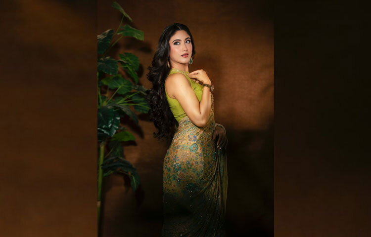 সঙ্গে মানানসই লাইম অলিভ রঙের স্লিভলেস হাই-নেক ব্লাউজে সোনালি জড়িসুতা আর সূক্ষ্ম সিকুইনের কাজ যুক্ত হয়ে দিয়েছে নিখুঁত রাজকীয় ফিনিশ। পুরো সাজেই ধরা দিয়েছে নারীত্বের এক নরম অথচ শক্তিশালী প্রকাশ।